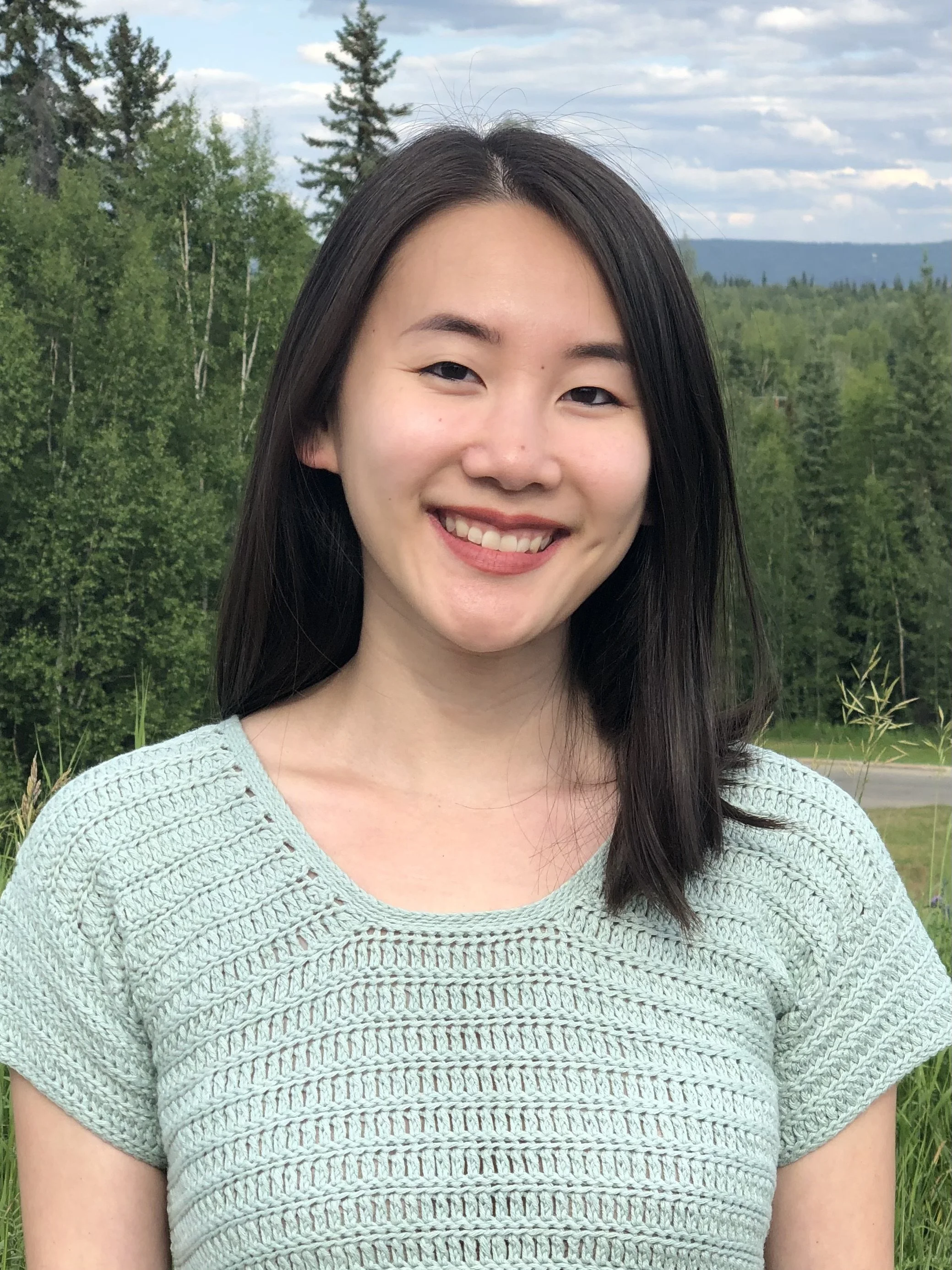 An Asian woman smiling in a green top with a forest background.