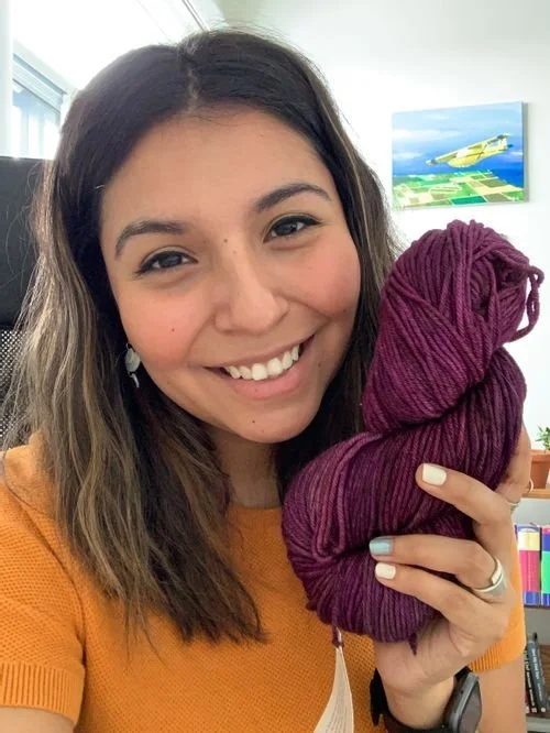 Maria Granados of MariasTejidos smiling and holding a skein of plum yarn