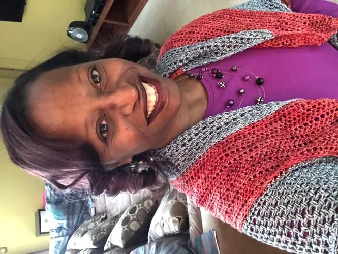 Freda Copeland of The Craft Den smiling in a coral and gray striped shawl over a purple top