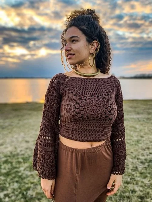 Fides Jo-Marie of AZRAMATI in a brown granny-square crop top by the water at sunset