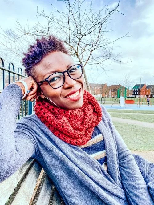 Kunbi Ayo-Okanlawon of Handmade by Kunbi in glasses and a red crochet cowl, outdoors