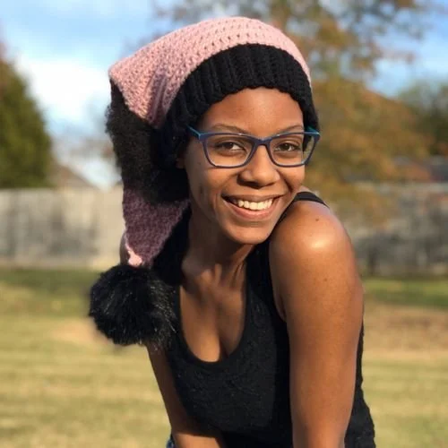 Mahala Kwanisai of Mahala Makes smiling in a long pink and black stocking cap