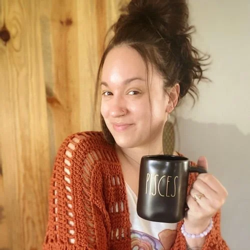 Tessa Herra of Tzigns in a rust crochet cardigan, holding a black mug