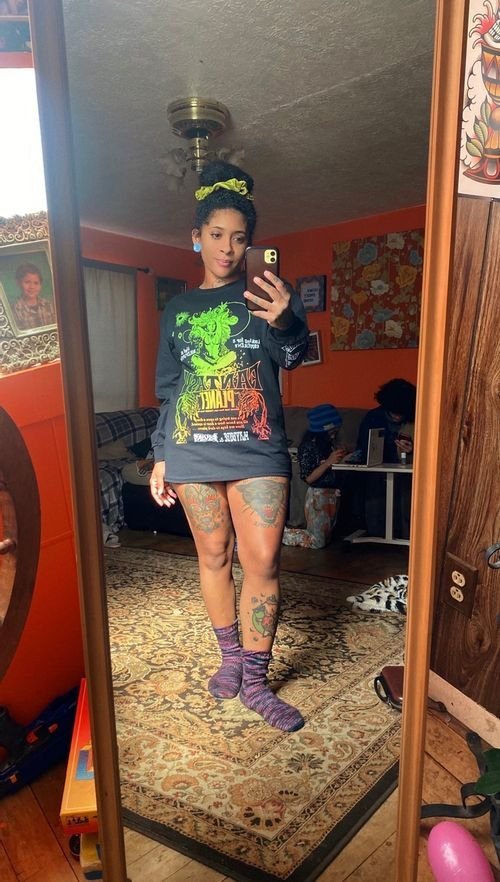 Nina Hudson of Brujeria Lana taking a mirror selfie in a graphic tee and patterned socks