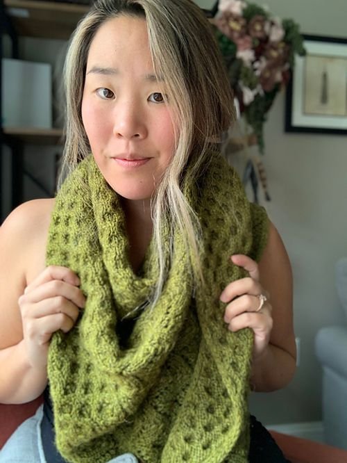 Sunnie Ko of Noodlyknits holding up a moss green chunky lace knit cowl