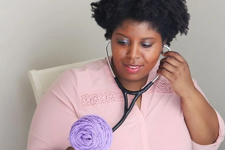 Laeia Jackson of The Crafty MD with a stethoscope and a ball of lavender yarn