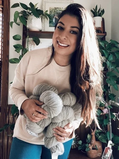 Yesenia Gutierrez of Seniyastudio smiling with an armful of gray yarn skeins