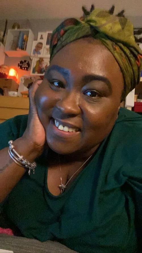 Rachel Barrett of FLYY Dyed smiling, chin in hand, in a green patterned head wrap