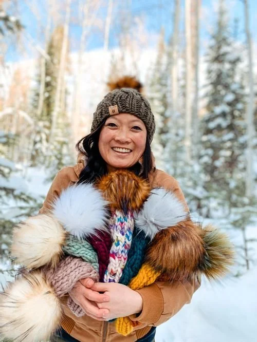 Chereen Leong Schwarz of Smeeny Beanie Knits holding an armful of pom-pom beanies in the snow