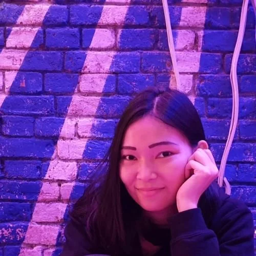 Sally Yanita of murasakiXIA smiling against a purple-lit brick wall
