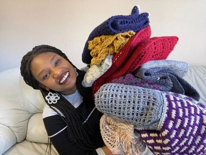 Andrea Pettaway of Drea's Hook smiling with an armful of colorful crochet pieces