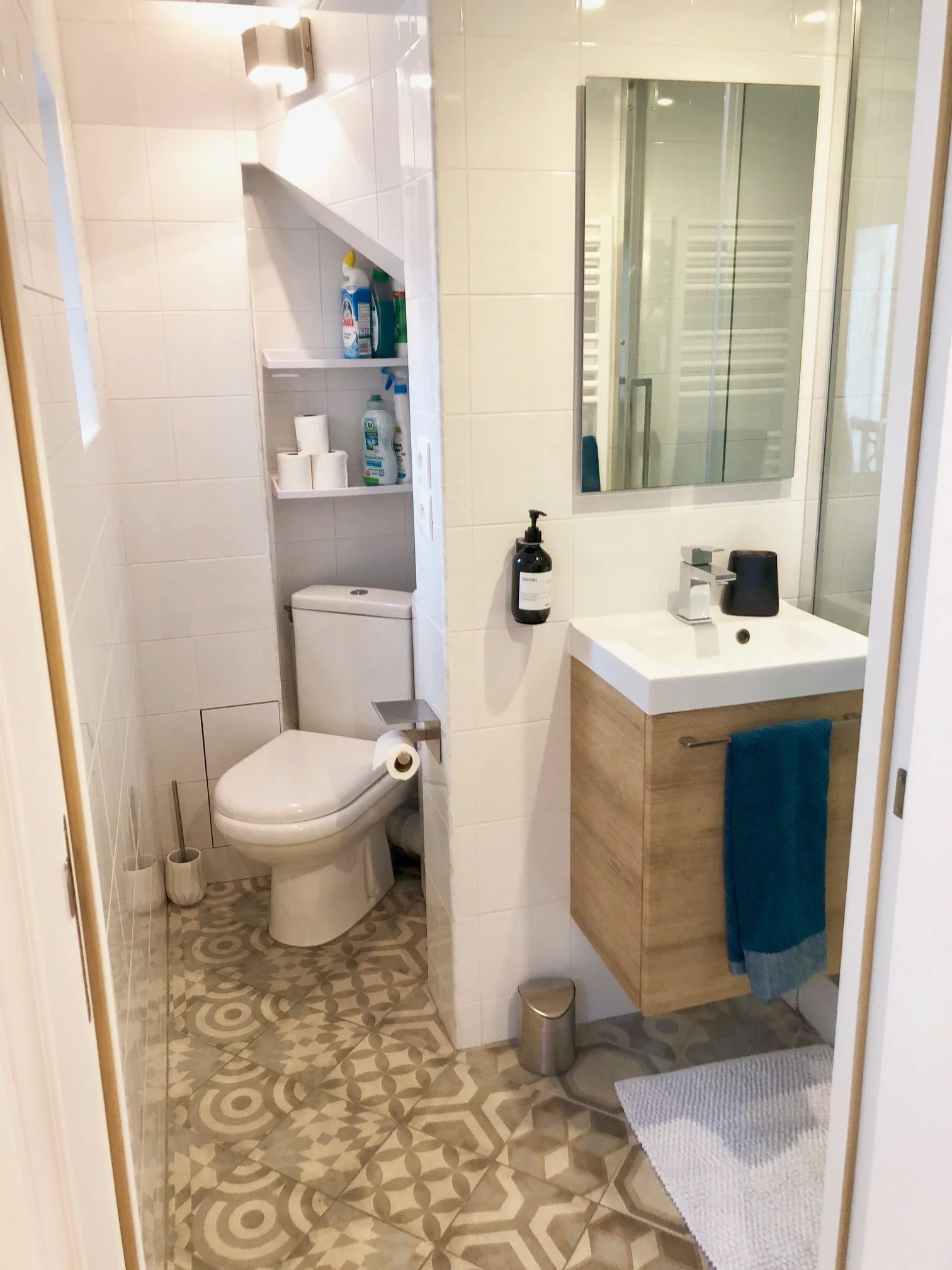 A small modern bathroom with a patterned tile floor, a white toilet, a white sink with a mirror above, and a shower with a glass door.