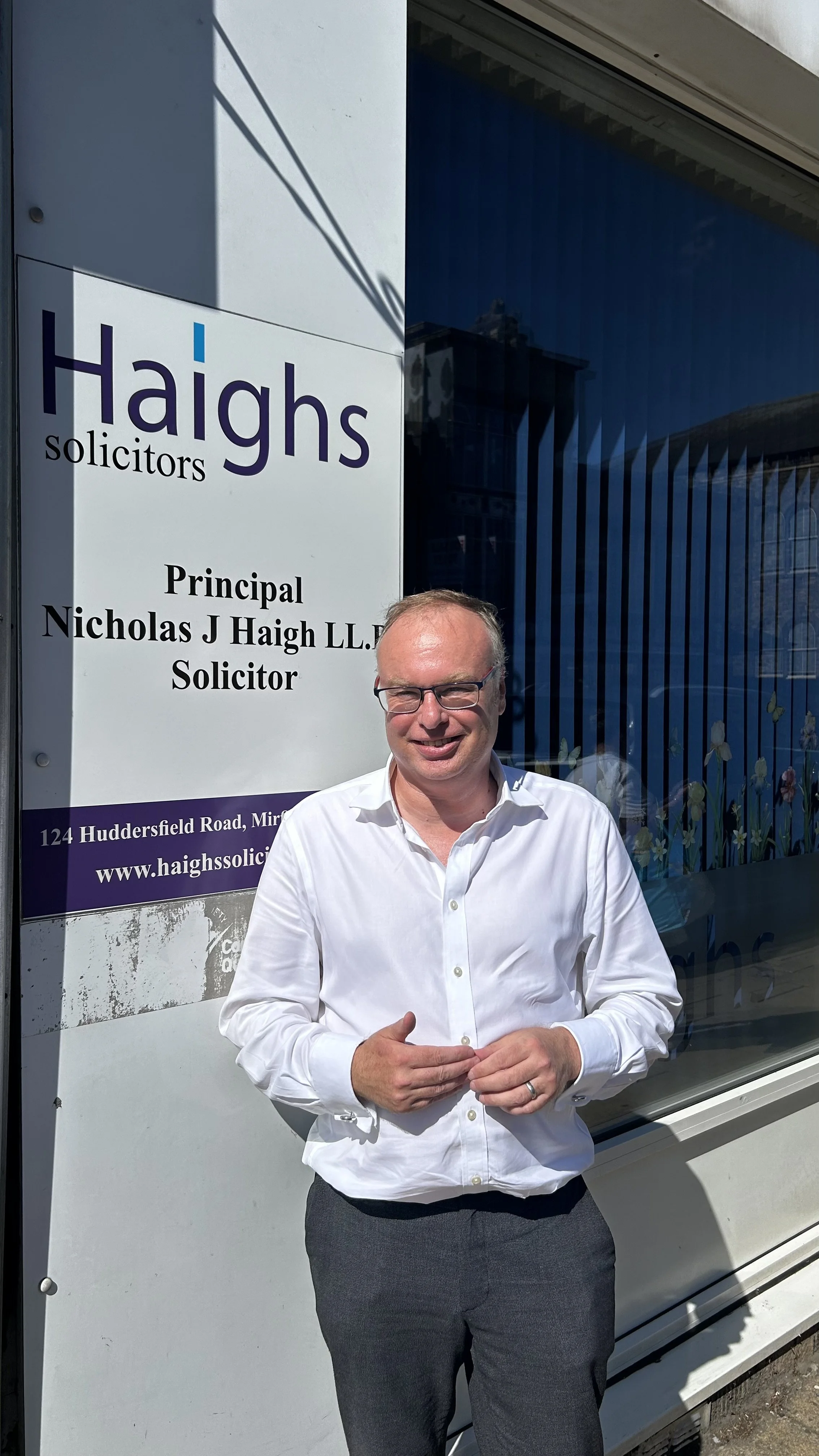 Nick Haigh solicitor outside office smiling in white shirt and wearing glasses in the sun of Mirfield West Yorkshire