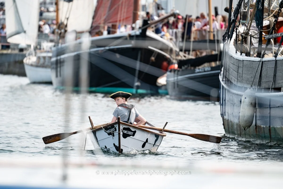 Jeune garçon sur sa barque au milieu des vieux gréements