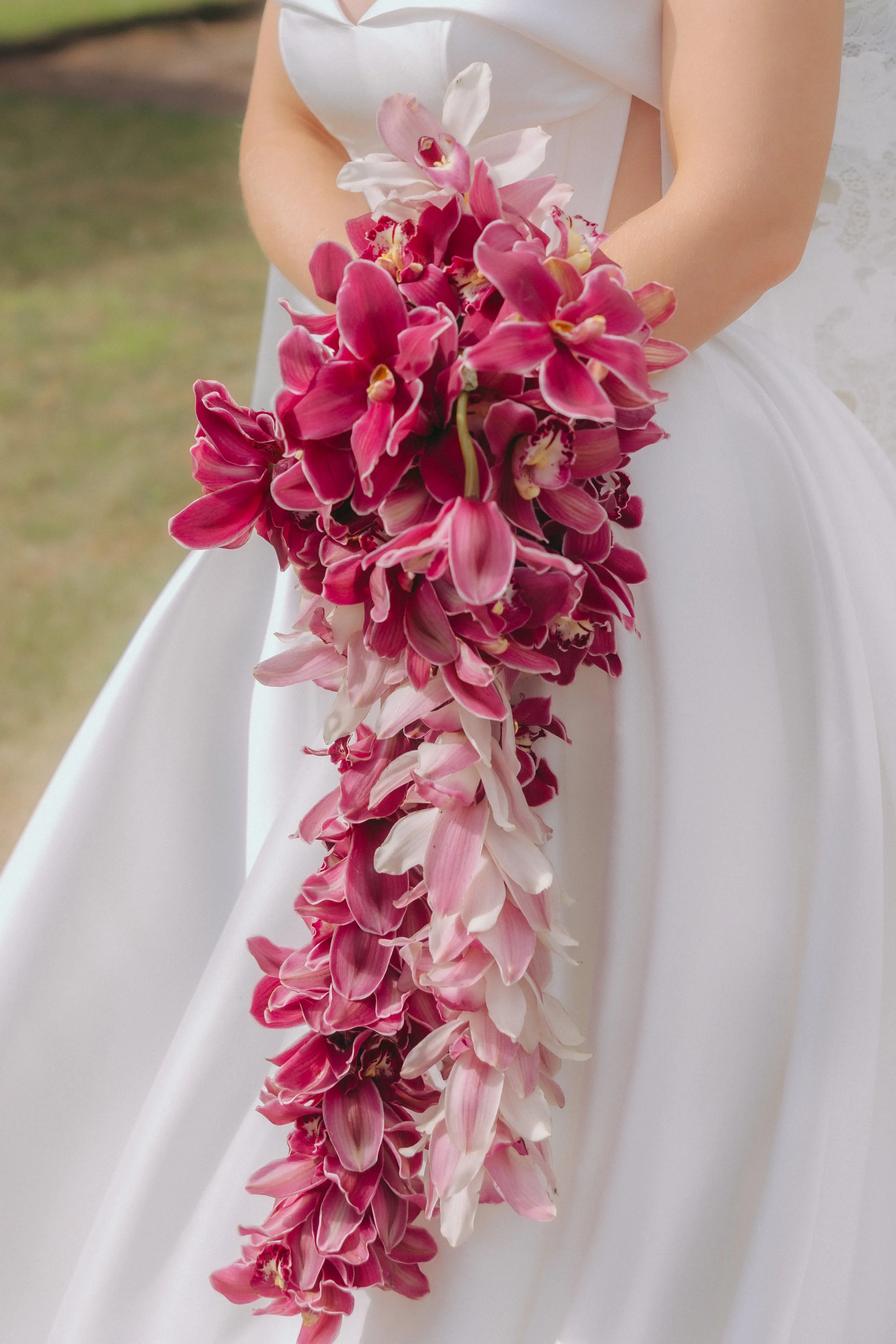 A woman in a white dress holding a cascading bouquet of pink and white orchids.