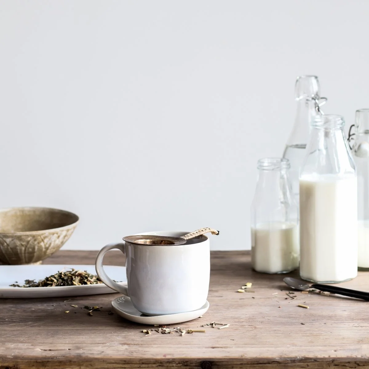 Tasses, bouteilles de lait, bol en céramique et cuillère sur une table en bois, ambiance café ou thé.