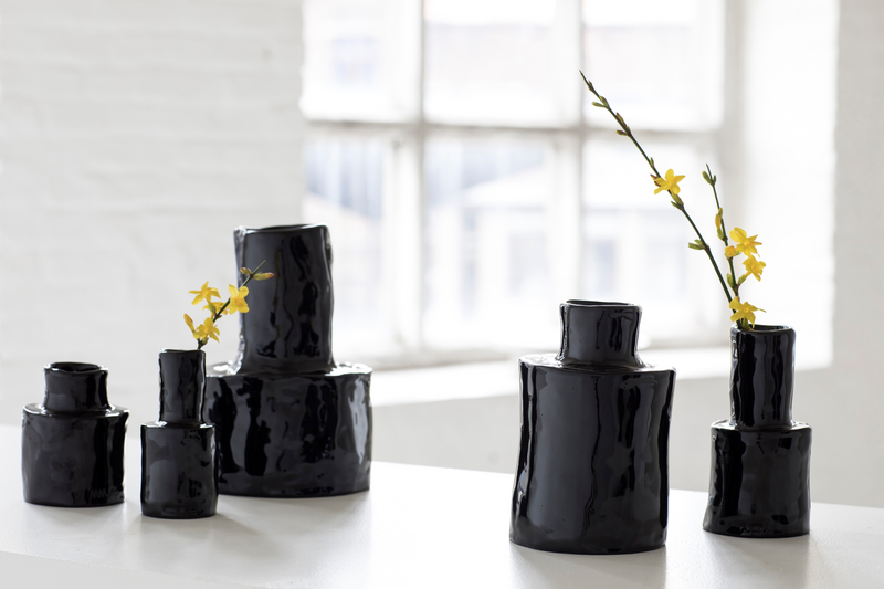 Vases noirs de différentes tailles avec des fleurs jaunes, disposés sur une table près d'une fenêtre