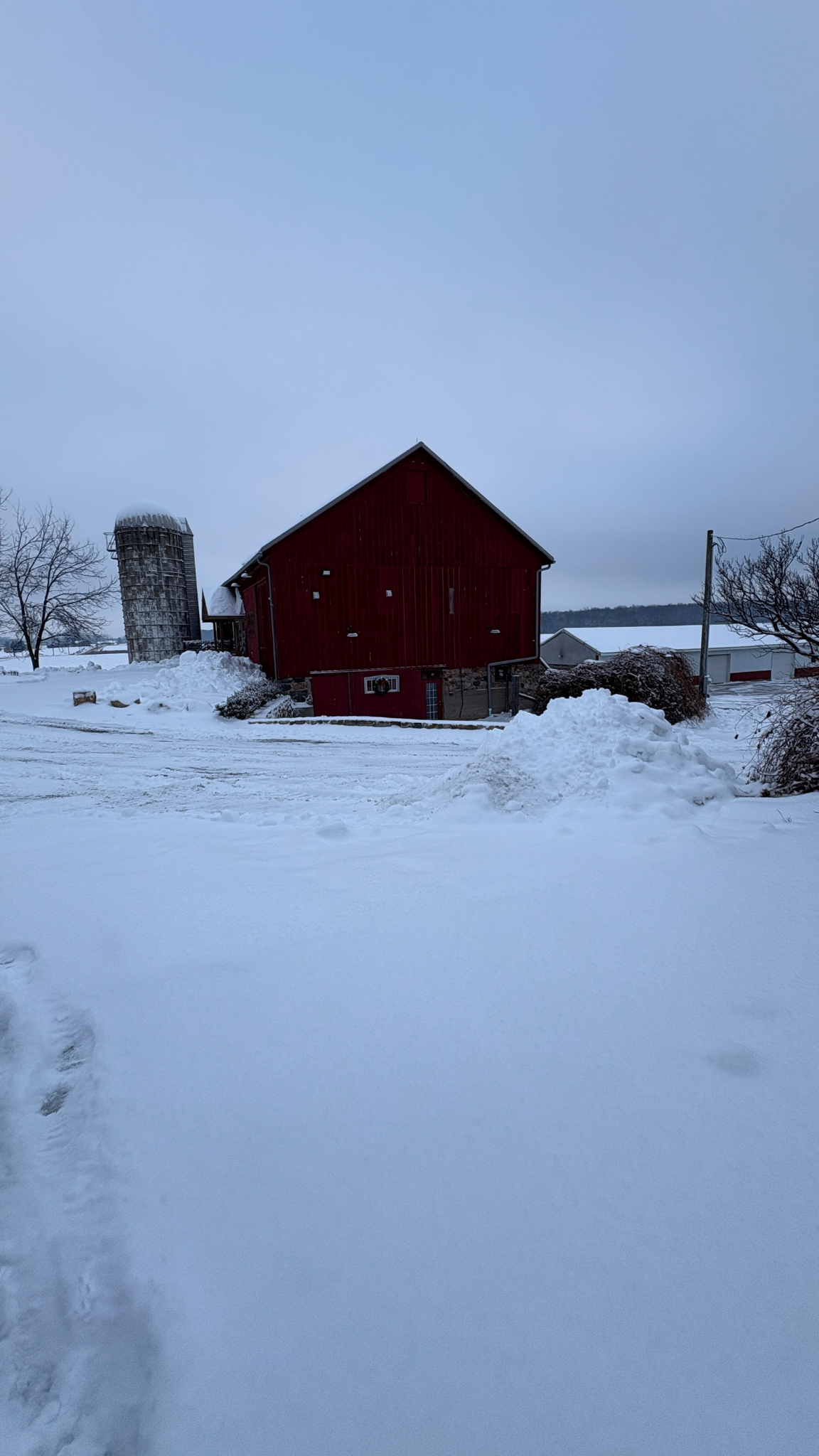 A red barn in a snowy landscape with a silo on the left and power lines on the right.