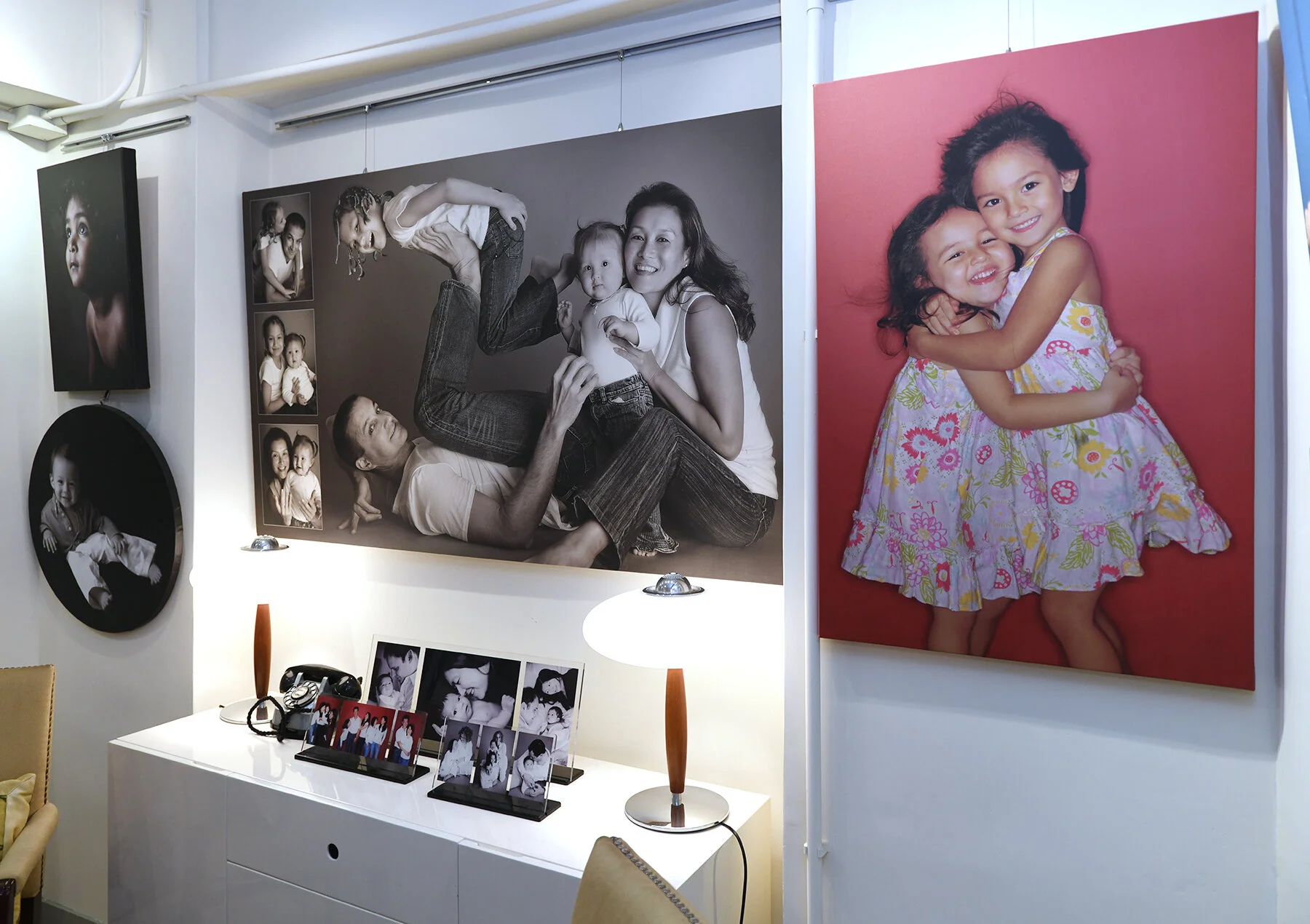 Interior room with wall-mounted family portraits and photo frames on a cabinet, featuring adults and children.