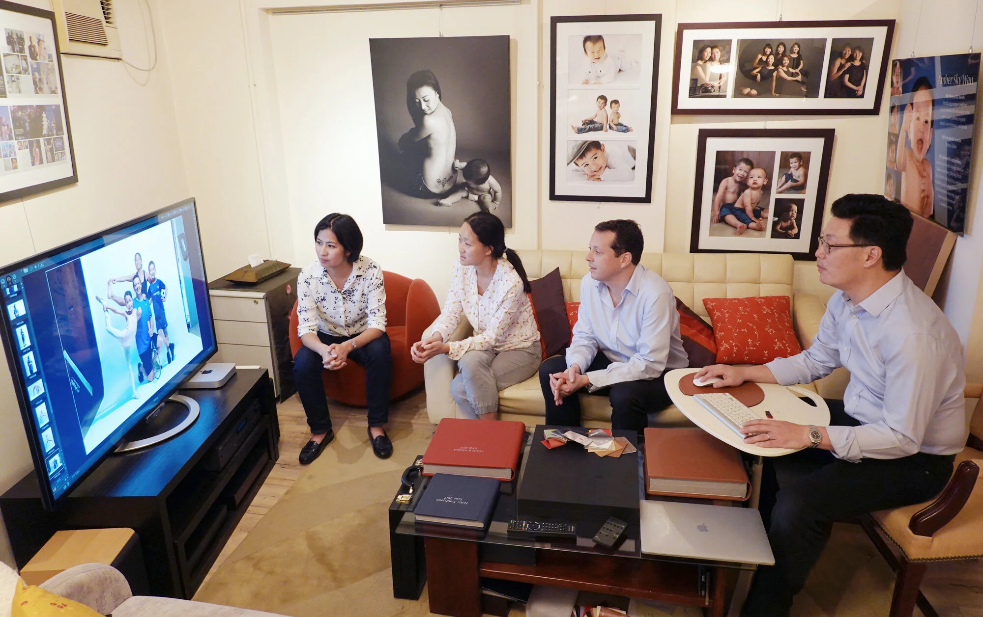Four people sitting and reviewing photos on a large screen in a room with framed portraits on the wall.