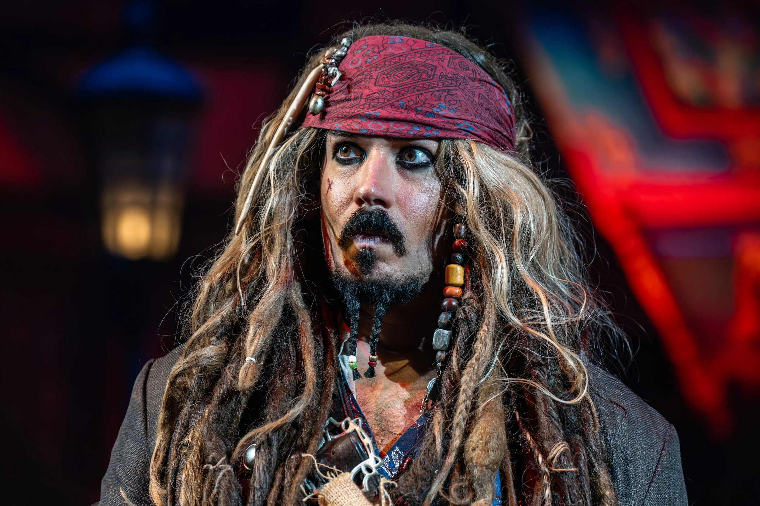 A person dressed as Jack Sparrow from Pirates of the Caribbean with long dreadlocks, a red bandana, and pirate attire.
