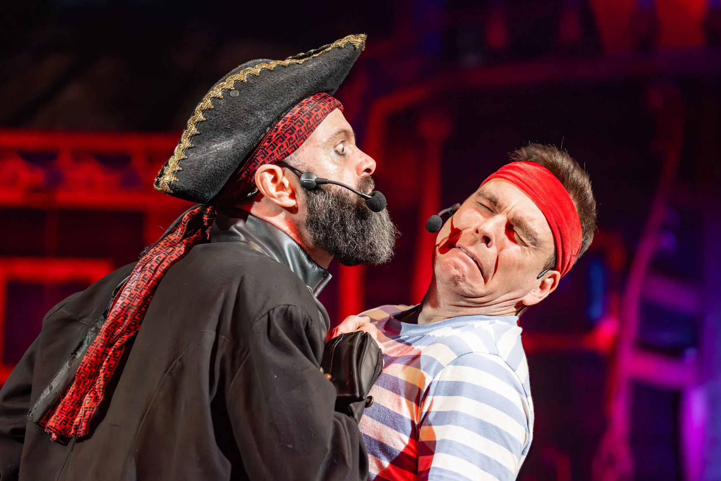 Two actors performing on stage, dressed as a pirate and a sailor, in a theatrical play.