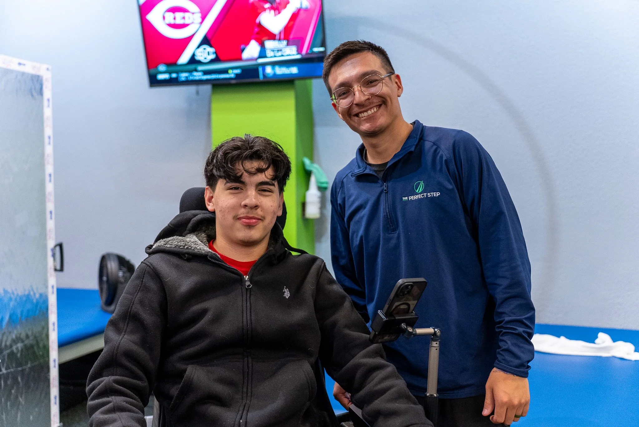 Two men, one in a wheelchair, smiling in an indoor setting.