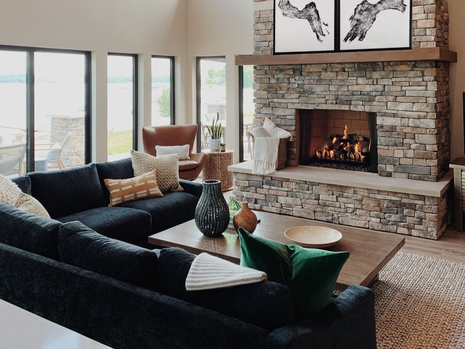  leather chair, stone fireplace, navy sectional, black windows, neutral paint, accessories, chandelier, artwork 