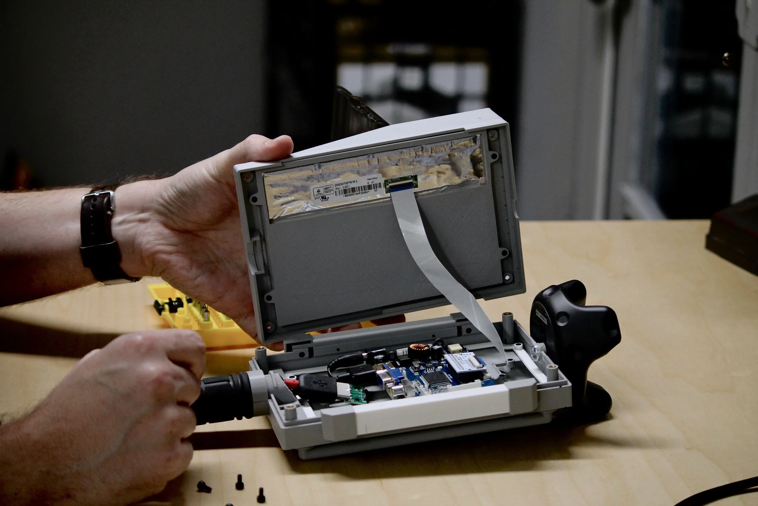 Person's hands putting together a handheld digital device with screws and electrical components showing