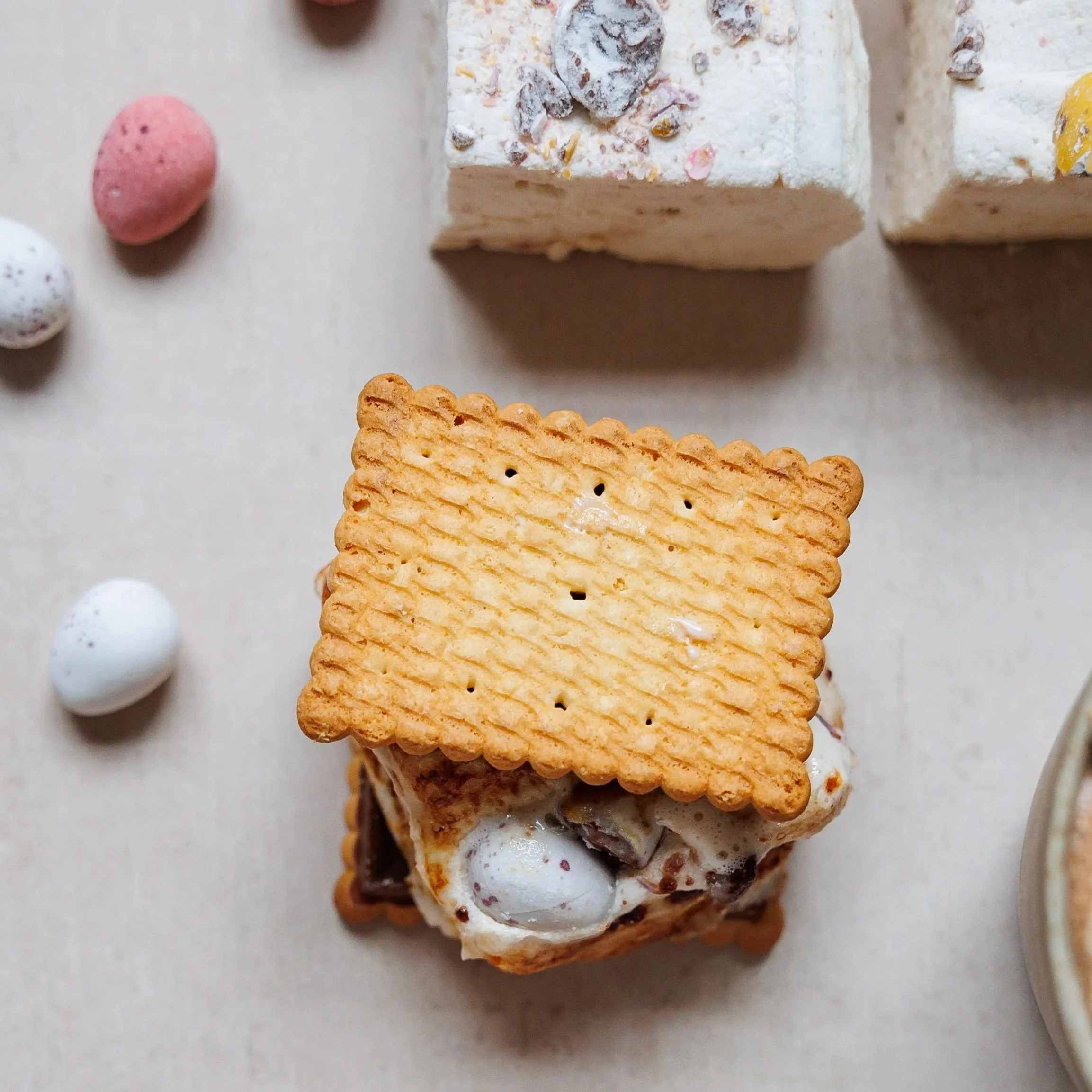 looking+down+on+a+biscuit+with+a+toasted+marshmallow+and+cadbury+mini+eggs+surrounded+by+marshmallows+and+with+mini+eggs+scattered+around+on+a+marble+table+top.jpg