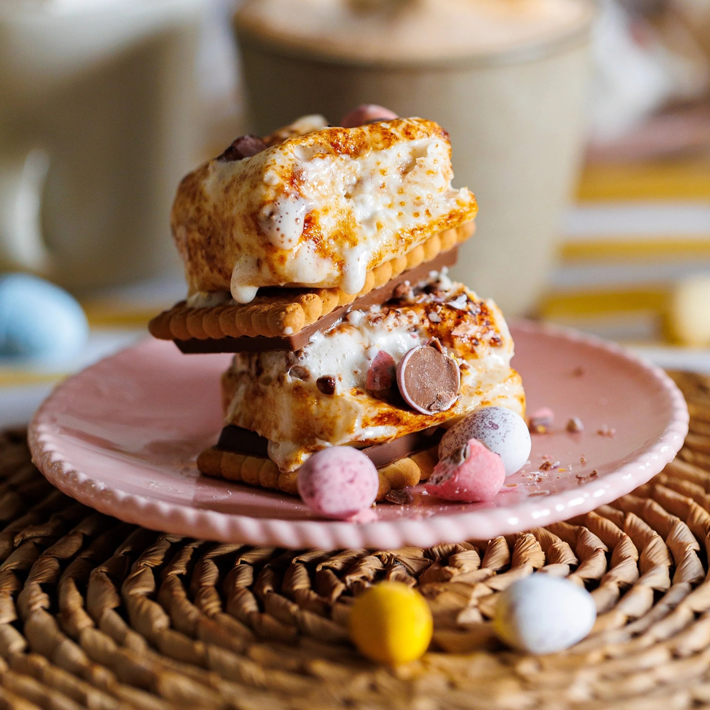 Toasted+marshmallows+and+mini+eggs+stacked+between+biscuits+on+top+of+a+pink+plate+on+a+wicker+place+mat.jpg