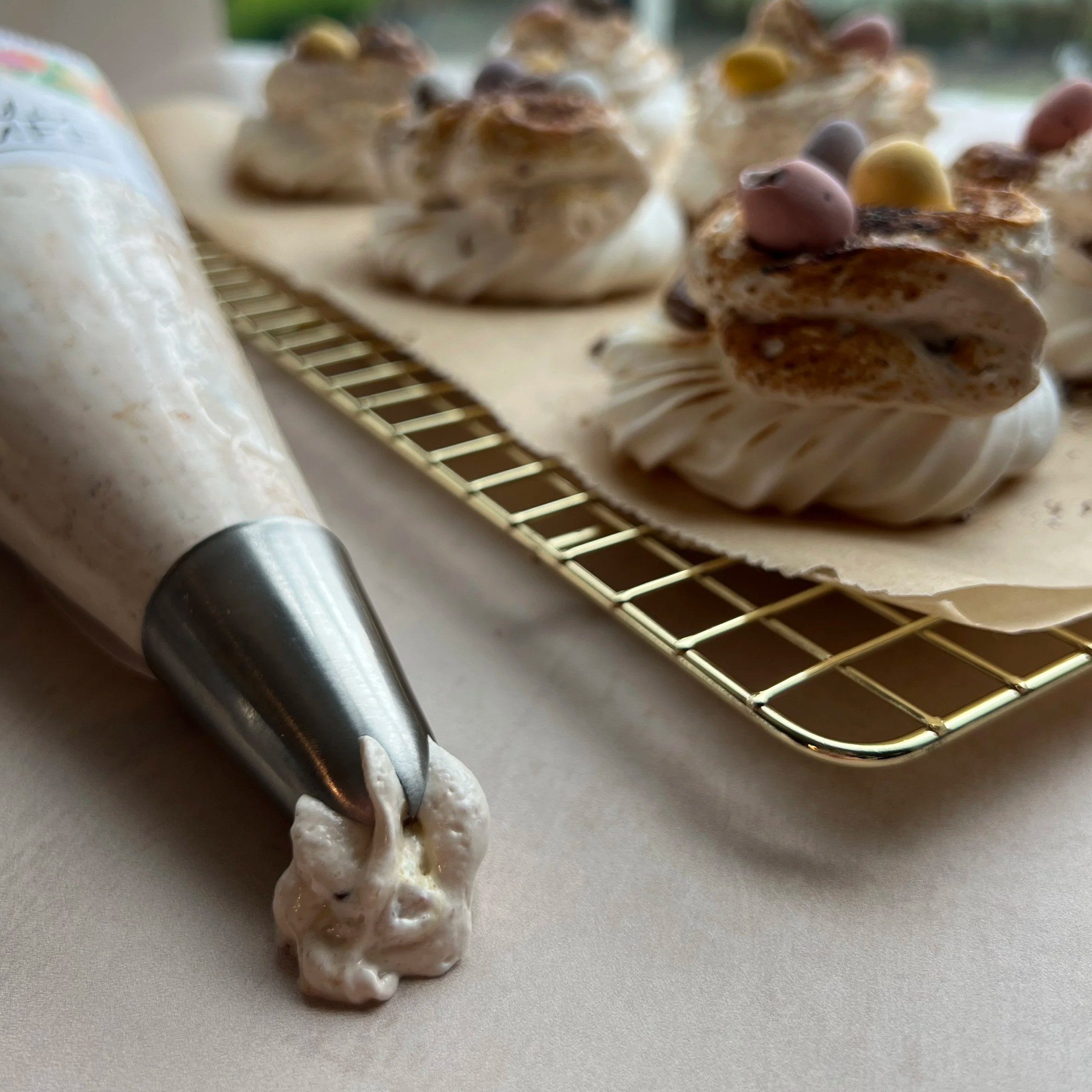 Close+up+of+piping+nozzle+with+Mini+Eggs+Wonder+Fluff+beside+a+baking+rack+with+meringue+nests+decorated+with+marshmallow+fluff+and+Mini+Eggs.png