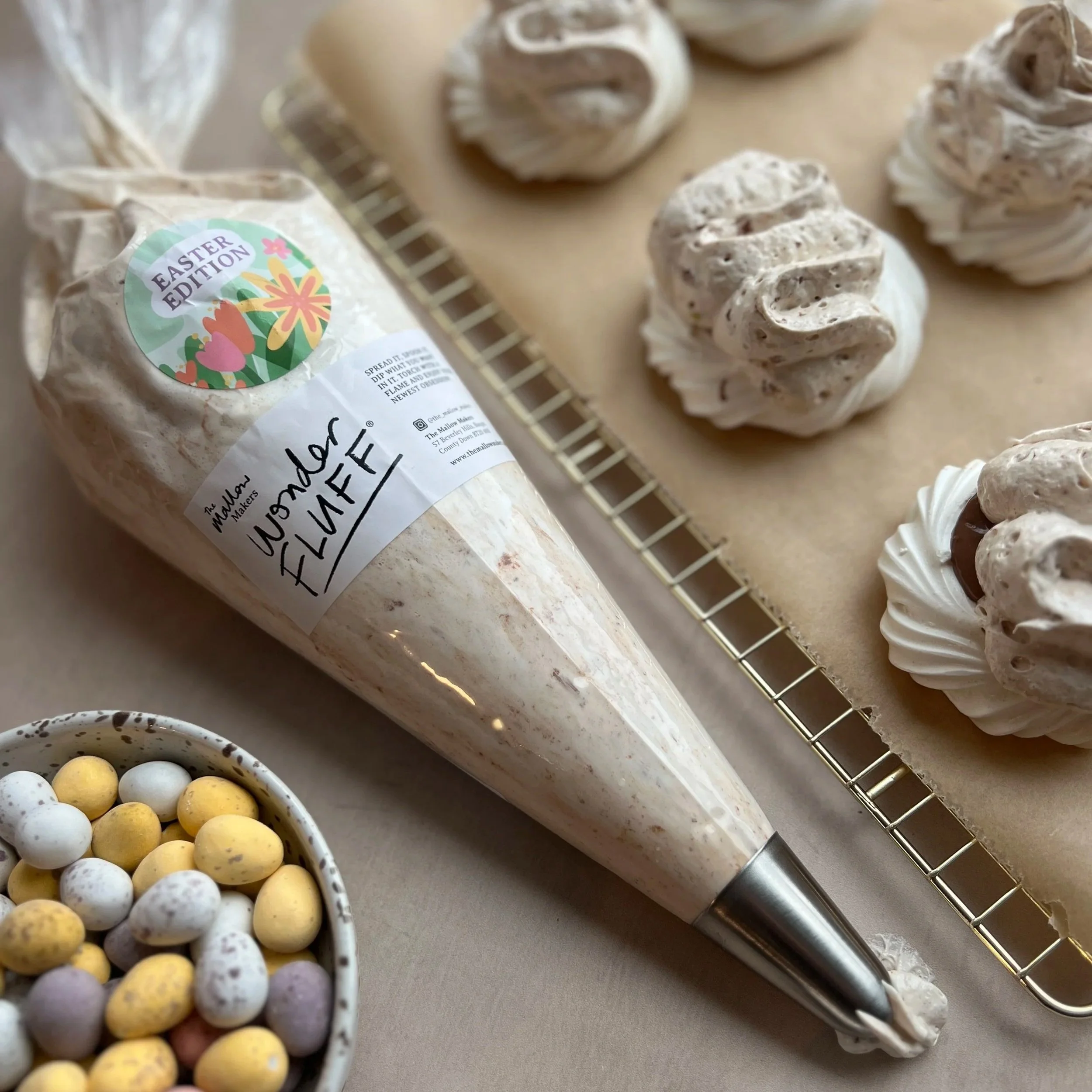 Mini+Eggs+Wonder+Fluff+in+a+piping+bag+with+fluff+coming+out+of+piping+nozzle+with+decorated+meringue+nests+in+the+background+and+a+bowl+of+mini+eggs+in+front.jpg