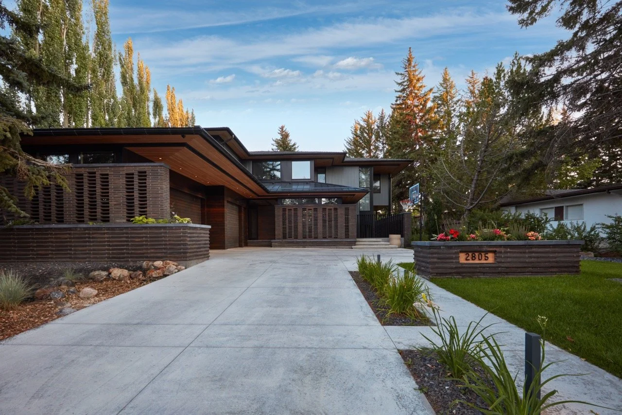 Modern house with a concrete driveway, wooden exterior, surrounded by trees and landscaped garden with flowers, and house number 2805.