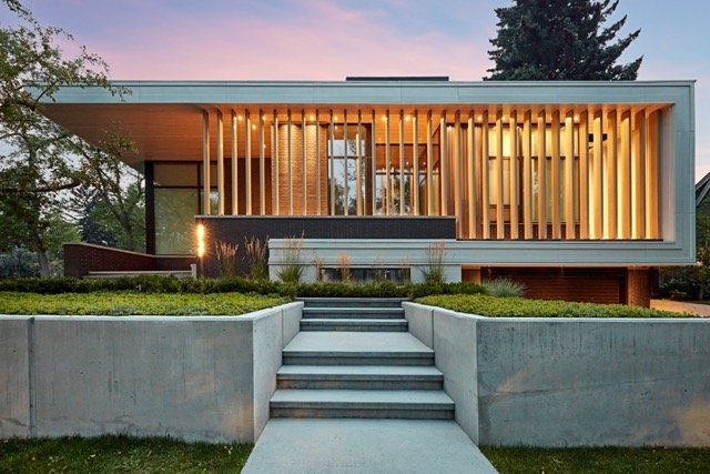 Modern two-story house with large vertical wooden slats, concrete facade, and landscaped yard.