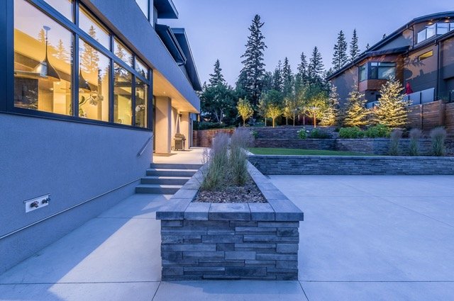 Modern backyard with concrete patio, stone planters, and trees.