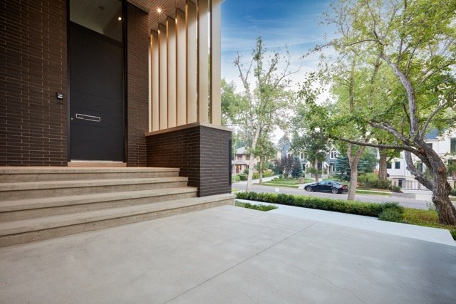 Modern house entrance with steps and a large porch, surrounded by trees and suburban neighborhood view.