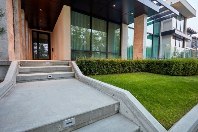 Modern house entrance with concrete steps, glass windows, and manicured lawn.