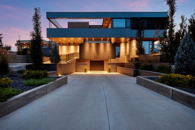 Modern luxury house with large driveway at dusk, featuring sleek architecture, illuminated entrance, and landscaped surroundings.