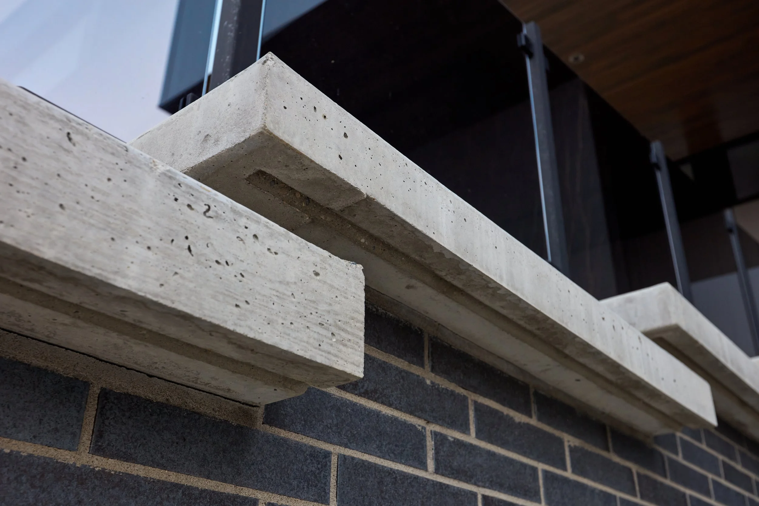 Close-up of layered concrete and brick wall with black metal shelving above.