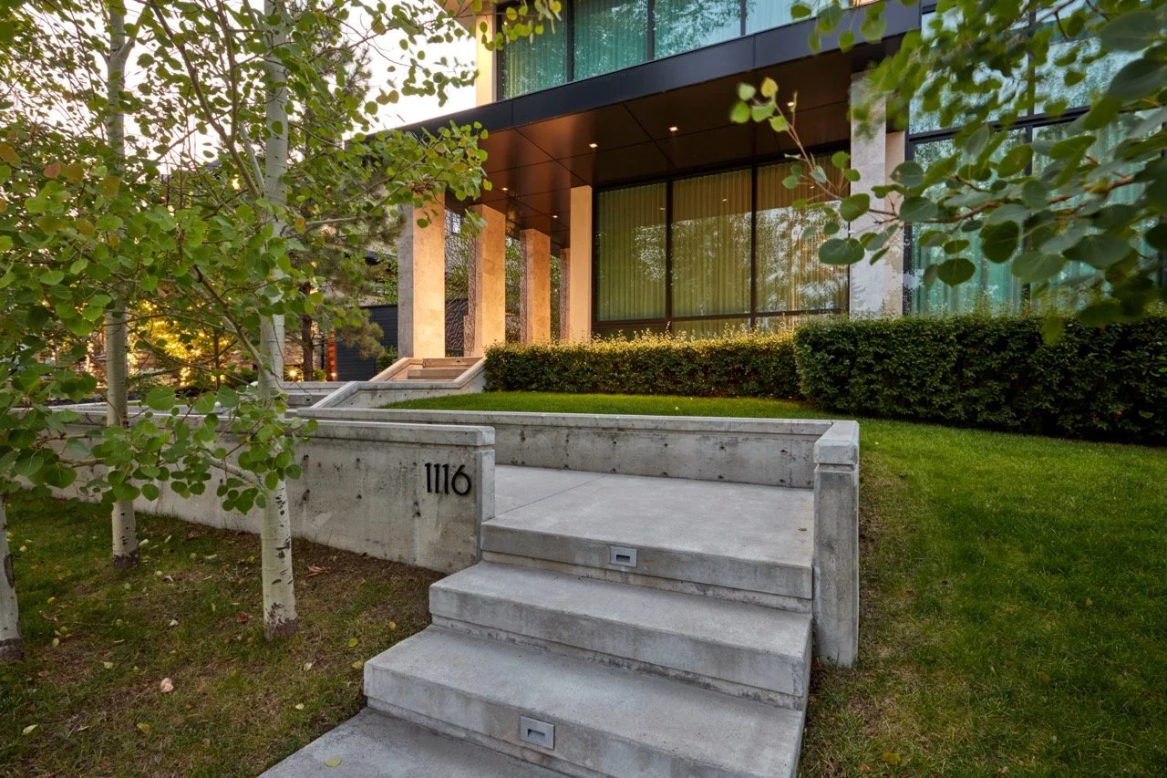 Modern building entrance with concrete steps, stairs, and a garden with trees and bushes in front.