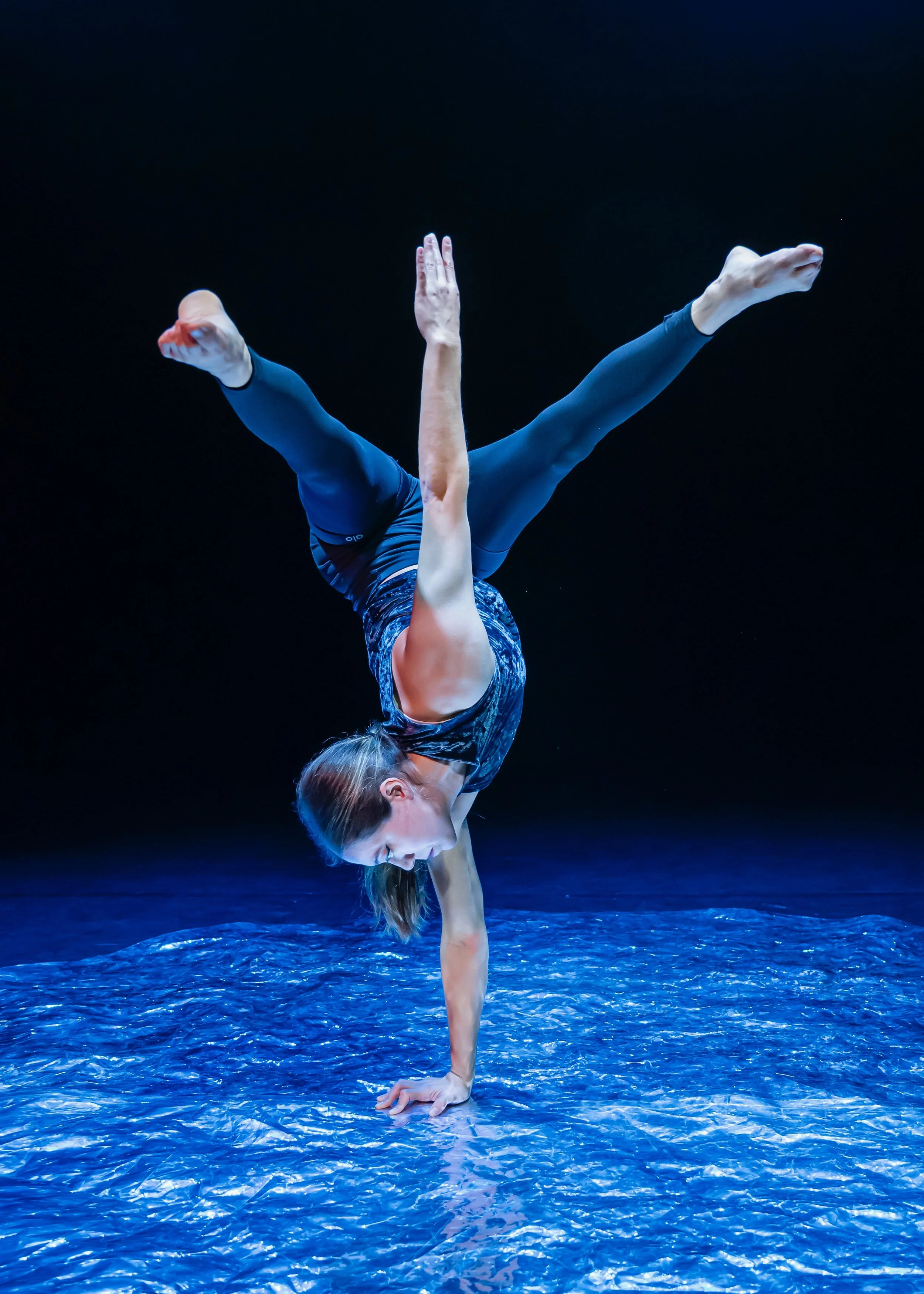 A woman performing a handstand on a blue textured surface with a dark background.
