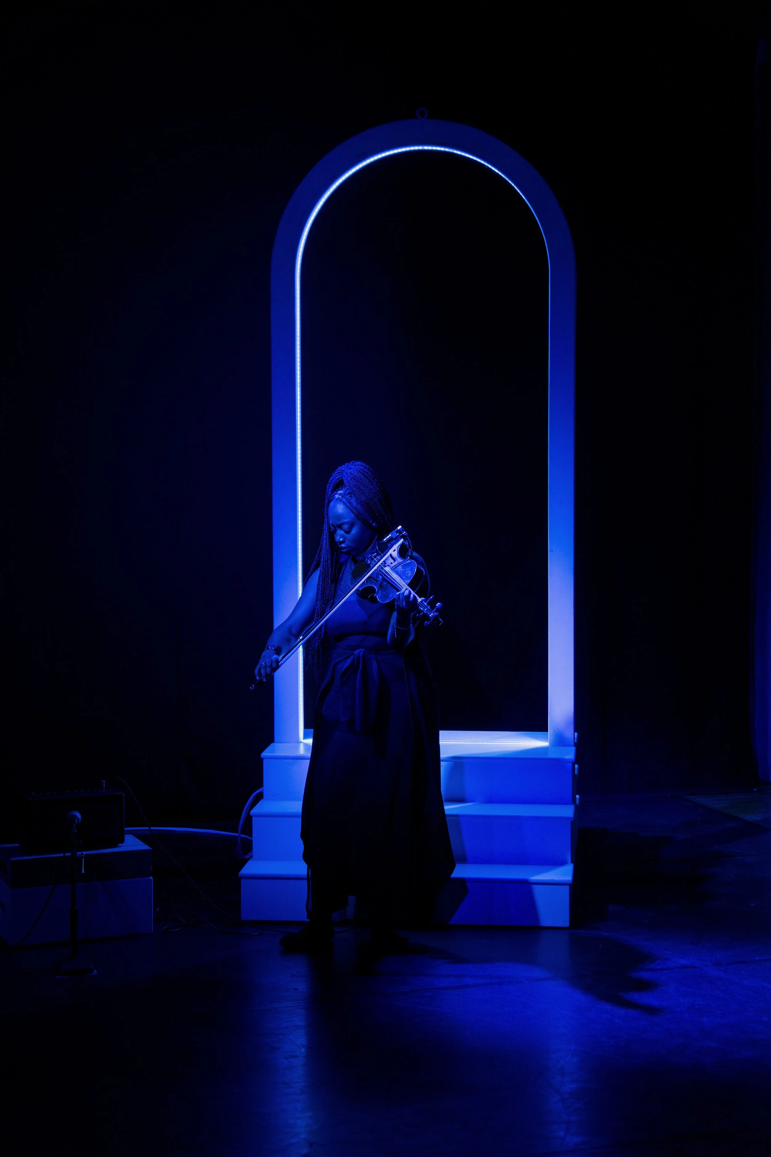 A woman playing a violin on a stage with blue neon lighting and a white arch backdrop