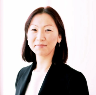 Professional woman with shoulder-length black hair, wearing a dark blazer and white top, smiling softly against a plain white background.