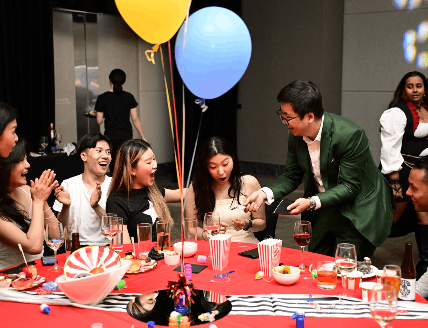 A magician performing a card trick at a formal event, with guests watching at a decorated banquet table.