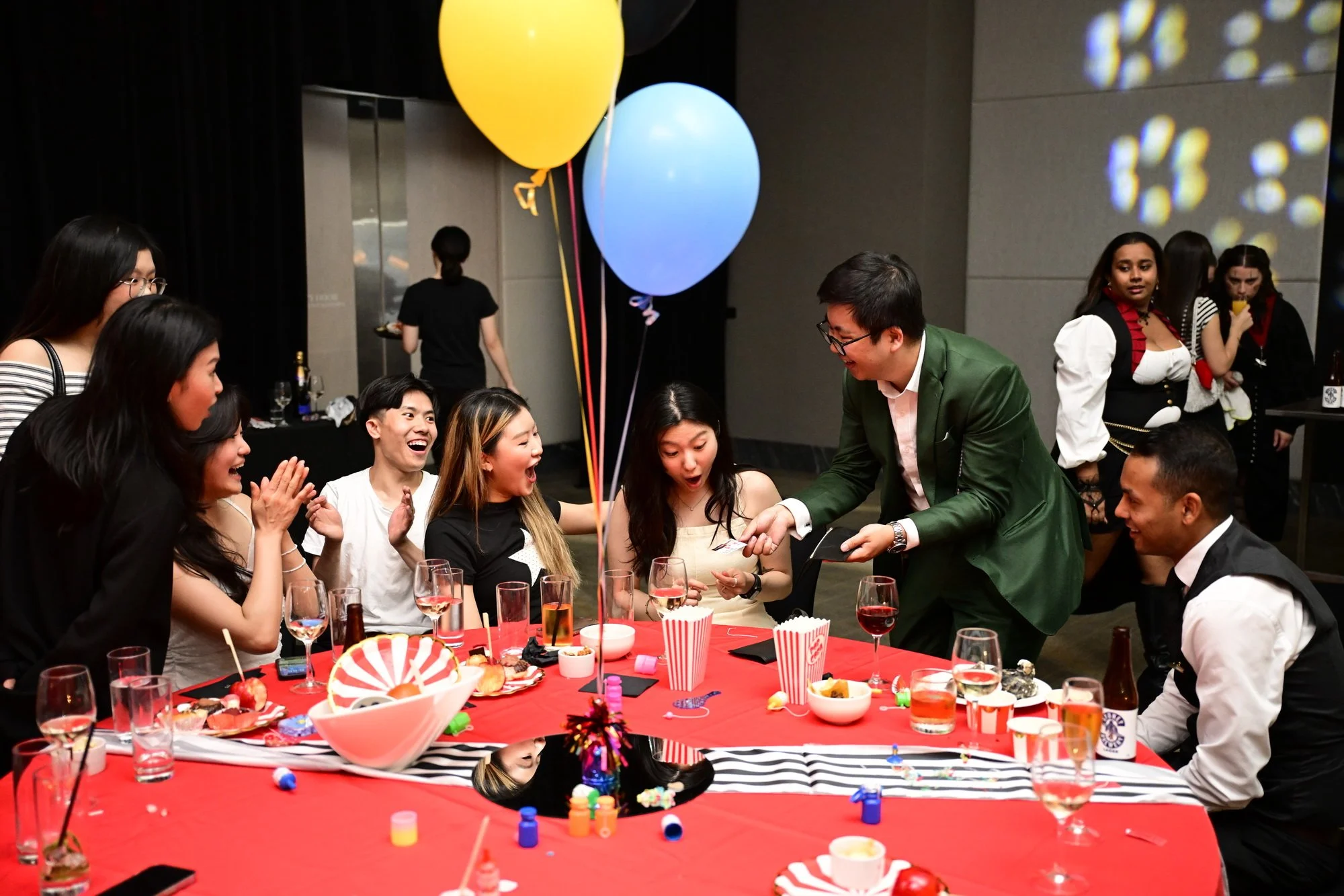 A magician performing a card trick at a formal event, with guests watching at a decorated banquet table.