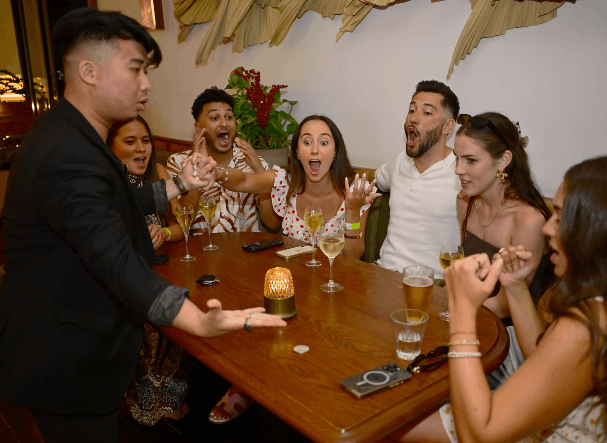 A Sydney magician dressed in a tuxedo with a bow tie, wearing white sneakers, standing on a stage in a dimly lit venue with musical instruments and a sign that reads 'Chaltime' in the background. The individual appears to be posing or performing.