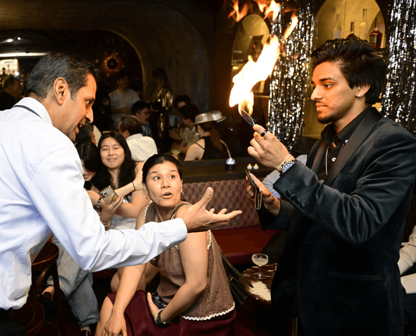 Group of people celebrating with a sydney magician at a wedding reception, with one man being lifted and others smiling and laughing, in a decorated banquet hall.