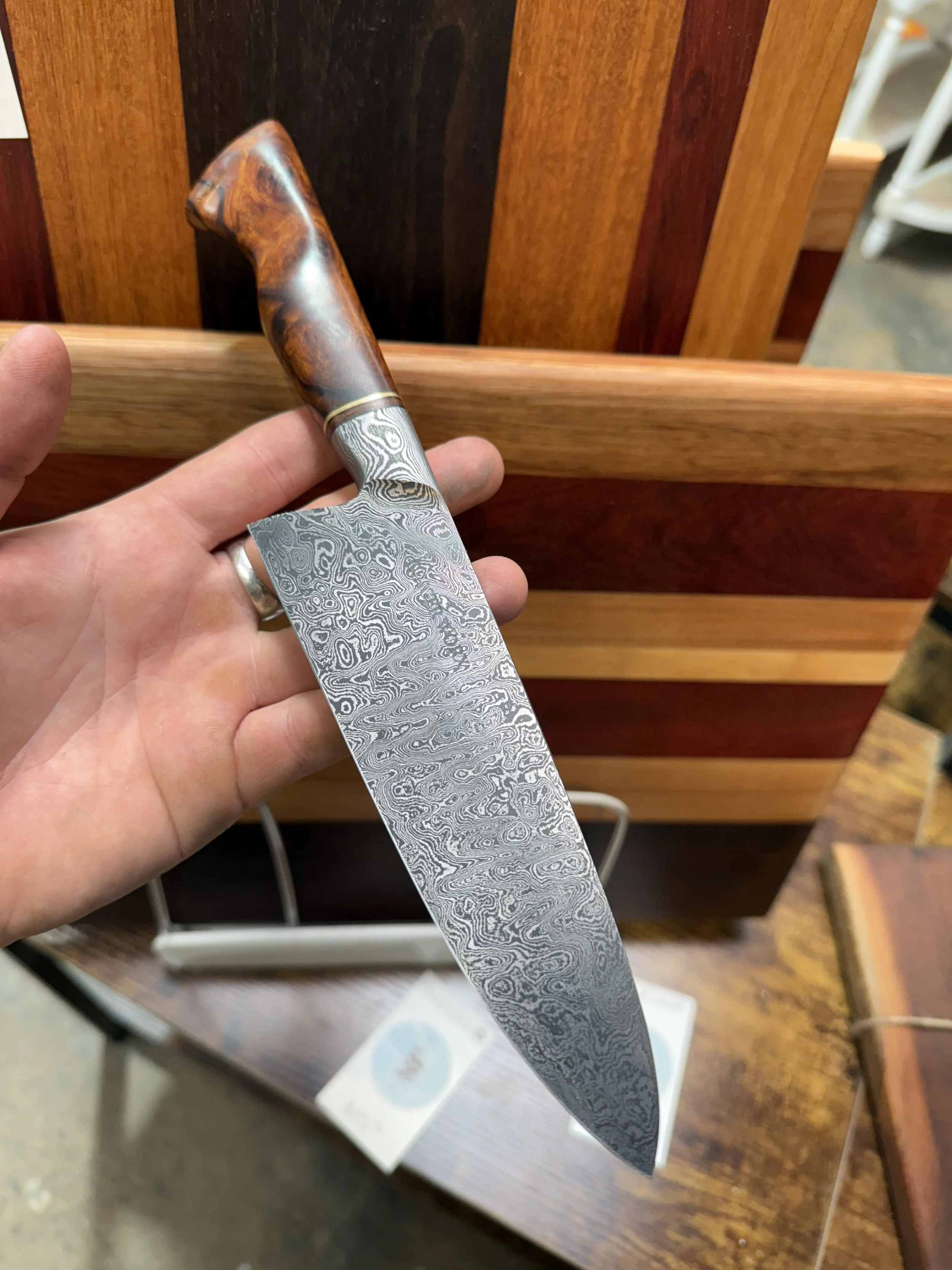 A person holding a Damascus steel kitchen knife with a wooden handle over a wooden counter.