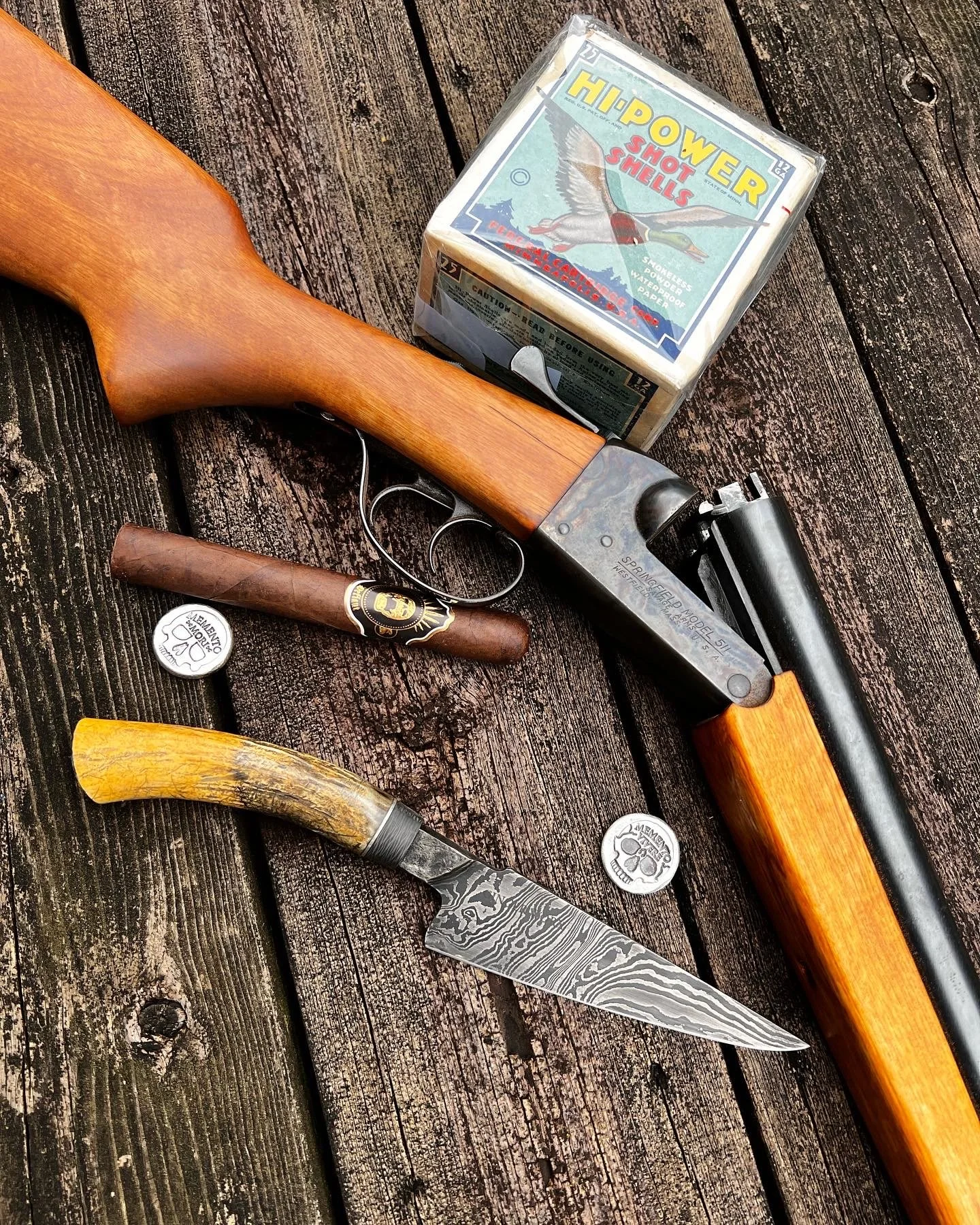 A wooden rifle, a folding knife with a bone handle, playing cards, a cigar, and two coins are displayed on a weathered wooden surface.